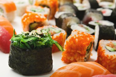 Çeşitli suşi dürümleri beyaz bir tabakta farklı renkler ve malzemeler sergiliyor. Bazıları deniz yosunu içerirken, bazıları parlak turuncu veya pembe malzemeler içerir..
