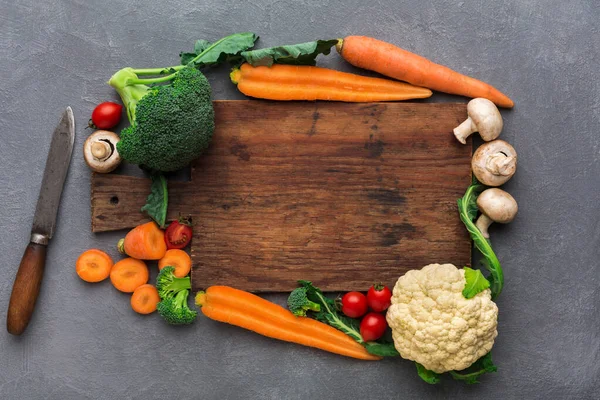 Taze sebzeler mutfak ortamındaki ahşap bir kesme tahtasının etrafına konur. Havuç, brokoli, karnabahar ve mantar kullanıma hazır bir bıçakla birlikte görülebilir..