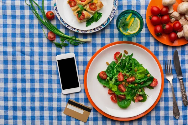 Yeşillik ve kiraz domatesinden yapılmış bir salata bir tabakta servis edilir. Limonlu bir içki yakınlarda durur. Masada bir telefon ve bir de kart var, diğer yiyeceklerle birlikte..