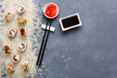 Suşi dürümleri, pirinçle çevrili gri bir yüzeye yerleştirilir. Küçük bir tabak soya sosu içerirken, zencefil ve çubuk turşusu yakında. Bu sahne bir yemek düzenini yakalar..