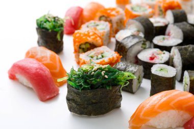 Suşi seçimi beyaz bir yüzeyde sergilenir. Çeşitli ekmekler ve deniz ürünleri görülebilir. Düzenleme, canlı renklere ve dokulara sahip farklı suşi türlerini içerir..