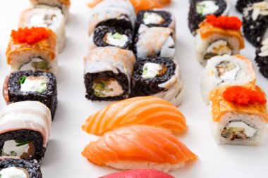 Farklı türde suşiler bir tabakta düzgünce düzenlenir. Seçimde balık, krem peynir ve sebzeli dürüm yer alıyor. Ekmeğin yanında çiğ balık parçaları var..