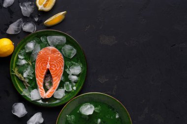 Taze bir somon filetosu buzla dolu yeşil bir tabakta oturur. Yanında biraz buz ve limon dilimleri var. Bu da yemek pişirme ya da servis etme hazırlığını gösteriyor..