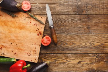 Taze sebzeler bir bıçağın yanındaki tahta kesme tahtasına dizilir. Tahtada domates, kabak ve yanına otlar konmuş patlıcan yer alıyor..