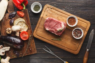 Taze sebzeler ve otlar bir et parçasıyla birlikte ahşap bir yüzey üzerinde düzenlenir. Baharat kaseleri koleksiyona renk ve tat katar. Bu düzen yemek hazırlığı için ideal..