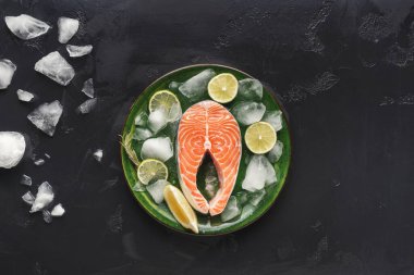 Somon fileto koleksiyonu buzla dolu yeşil bir tabakta duruyor. Limon ve limon dilimleri balığın etrafına konur. Ayarlar yiyecekleri temiz ve basit bir şekilde gösteriyor..