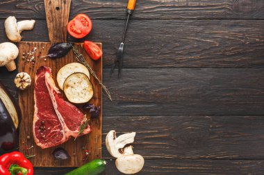 Bir kolaj yemek pişirmek için çeşitli taze malzemeler gösterir. Domates, kabak ve mantar gibi sebzelerin yanında bir parça et var. Eşyalar ahşap bir tahtaya dizilmiştir..