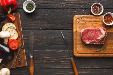 Taze sebzeler, otlar ve et kırsal bir ahşap masada düzenlenir. Bıçaklar ve kaseler yemek pişirmek için yakınlara konur. Bu sahne yemek hazırlıklarını gösteriyor..