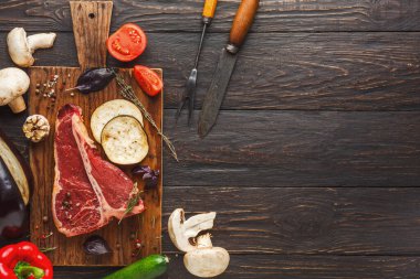 Et ve çeşitli sebzeler ahşap bir kesme tahtasına yerleştirilir. Sahnede kırmızı et, mantar, domates ve bitkiler gösteriliyor. Kesme araçları arka planda görünür.