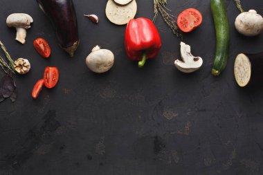 Kırmızı çan biberi, patlıcan, kabak, domates, sarımsak, mantar ve otlar da dahil olmak üzere taze sebzeler koyu bir yüzeye dizilmiştir. Bu kurulum yemek hazırlığı için hazır..
