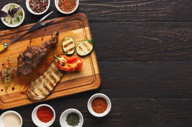 Ahşap kesim tahtasında ızgara et, dilimlenmiş kabak ve dolma biber bulunur. Tahtanın etrafında çeşitli baharat kaseleri var. Bu da yemek hazırlığını gösteriyor..