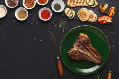 Izgara biftek yeşil bir tabağa konur. Etrafında da çeşitli baharatlar ve küçük kaplar vardır. Kara tahtada dilimlenmiş sebzeler var. Masa karanlık, yiyeceğe odaklanmamızı sağlıyor..