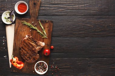 Izgara et ve taze sebze koleksiyonu bir mutfaktaki ahşap kesme tahtasının üzerinde düzenlenir. İçindekiler arasında baharatlar, bitkiler ve taze ürünler yer alıyor. Bu kurulum yemek pişirme etkinliğini vurgular.