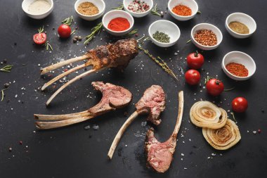 Çeşitli et kesimleri, çeşitli baharatlar ve taze domateslerin yanı sıra koyu bir yüzeye yerleştirilir. Bu düzenek yemek pişirmek için hazırlık öneriyor. Sahne hazır malzemeleri gösteriyor..