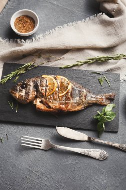 Izgara bir balık koyu bir tahta üzerine yerleştirilir. Etrafına taze otlar dizilir ve yakınlarda küçük bir tas baharat bulunur. Yemek için çatal ve bıçak hazır. Bu sahne bir yemek düzenini yakalar..