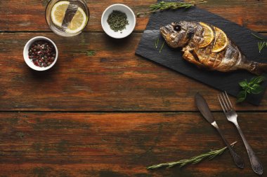 Bütün bir balık siyah bir levhada sunulur. Balıkların etrafını şifalı otlar ve baharatlarla çevrili. Yanında limonlu bir bardak su var. Sahnede kırsal ahşap bir masa var..