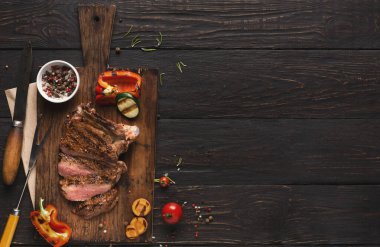 Dilimlenmiş sebzelerin yanında ızgara et parçaları tahtanın üzerinde duruyordu. Yanında küçük bir kase baharat duruyor. Sahne yemek hazırlıklarını gösteriyor..