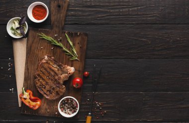 Izgara biftek, baharat ve taze sebzelerden oluşan bir koleksiyon. Mutfaktaki ahşap bir tahtaya dizilmiş. Ürünler arasında baharat, şifalı otlar ve biber var. Sahne yemek hazırlıklarını gösteriyor..