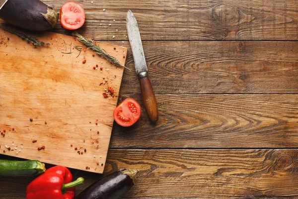 Taze sebzeler bir bıçağın yanındaki tahta kesme tahtasına dizilir. Tahtada domates, kabak ve yanına otlar konmuş patlıcan yer alıyor..