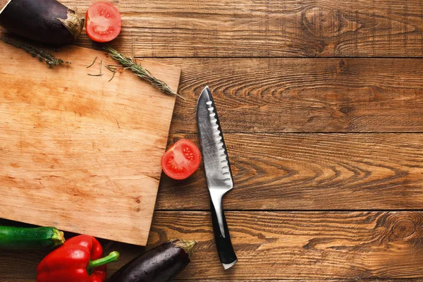 Tahta bir yüzeye taze sebze koleksiyonu yerleştirilir. Dilimlenmiş domateslerin yanında bir bıçak var. Sebzelerin canlı renkleri kahverengi ahşaba karşı duruyor..