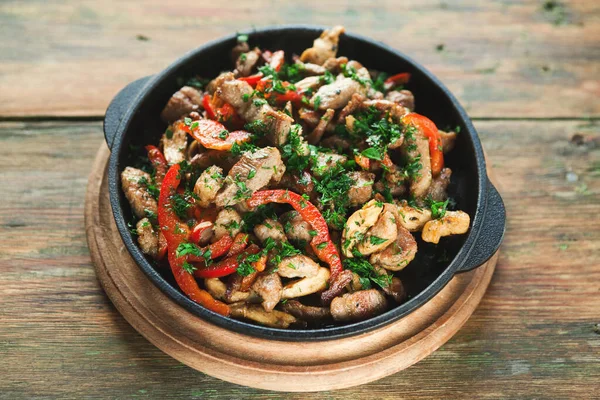 Renkli sebzelerle pişirilmiş etler ahşap bir masada bir tavada servis edilir. Yemekler otlar ve baharatlar içeriyor. Ayar gündelik ve davetkar..