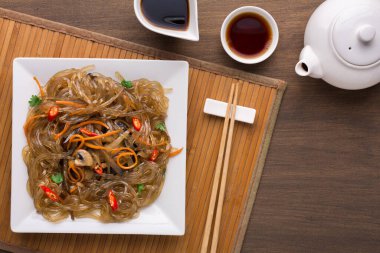 Kare tabakta sunulmuş erişte tabakları. Tabakta sebze ve baharatlı erişte var. İki küçük kase sos ve bir çaydanlık yakınlarda ahşap bir paspasın üzerinde oturur..