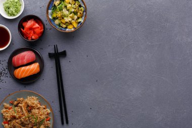 Farklı yemekler ve malzemeler bir masaya dizilir. Salata, sos ve dilimlenmiş sebzeler var. Suşi ve tavuklu bir tabak pirinç de dahil. Yemek çubukları yakınlarda dinleniyor..