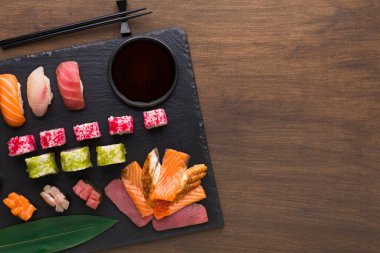 Siyah tahta üzerinde çeşitli suşi türleri düzenlenir. Farklı renkler ve şekillerde çiğ balık, pirinç ve sebzeler sergilenir. Çiftler arasında küçük bir kasede soya sosu ve yemek çubukları yer alıyor..