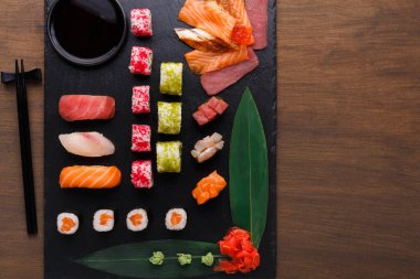 Bir suşi koleksiyonu siyah bir levhada sergilenir. Set çeşitli suşi türleri, sashimi ve süslemeler içermektedir. Yemek çubukları ve soya sosuyla düzgünce düzenlenmiş..
