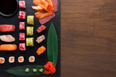 Siyah servis panosunda farklı suşi türleri sıralanır. Suşi dürüm ve sashimi içeriyor. Yeşil wasabi ve turşulu zencefil suşinin yanına yerleştirilir. Soya sosu küçük bir tabakta..