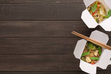 İki paket kutusu koyu ahşap bir masaya konur. Her kutuda renkli sebzelerle karıştırılmış erişteler var. Çubuklar kutuların yanında dinleniyor. Bu sahne basit bir yemek düzenini gösteriyor..