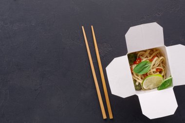 Erişteler limon ve fesleğenle servis edilir. İki tahta çubuk kutunun yanında dinleniyor. Masa karanlık, yiyeceğe odaklanmamızı sağlıyor..