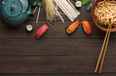 Suşi, erişte ve çay seti ahşap bir masada düzenlenir. Çubuklar ve malzemeler kasenin etrafına yerleştiriliyor ve Asya mutfağını gösteren mozaik bir görünüm yaratıyor..