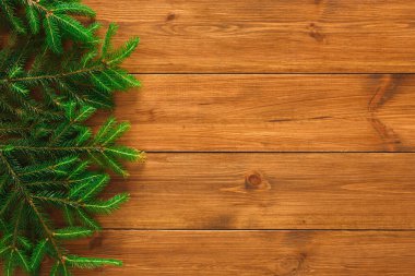 Ladin dalları ahşap bir yüzey boyunca sıralanır. Ayarlar tatil süslemeleri için hazırlık öneriyor. Ormanın sıcak tonları, yeşil dallarla tezat oluşturuyor..