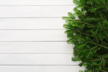 Bir Noel ağacının yeşil dalları kısmen beyaz ahşap bir yüzeye yerleştirilir. Düzenleme, temiz zemine karşı doğal yeşilliği gösteriyor. Bu da tatil temasını akla getiriyor..