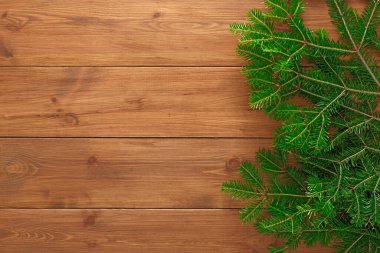 Kolaj, ahşap bir yüzeye yerleştirilmiş yeşil çam dallarını gösteriyor. Ayarlar basit bir düzende doğal dokuları ve renkleri vurgular. Bu sahne doğanın özünü yakalar..