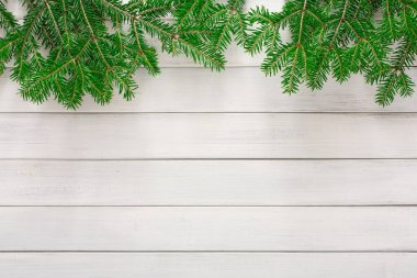 Yeşil çam dalları, açık ahşap bir yüzeyin tepesinde düzenlenir. Dallar doğal bir sınır oluşturuyor. Ortam kış ya da tatil temaları için uygundur ve biraz doğa katar..