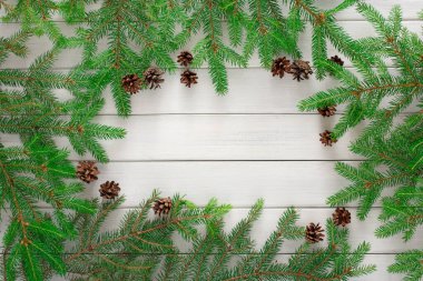 Çam dalları, ahşap bir yüzey üzerindeki bir alanı sarar. Düzenleme farklı boyutlarda çam kozalakları içeriyor. Bu tasarım mevsimlik dekorasyon veya zanaat için kullanılabilir.