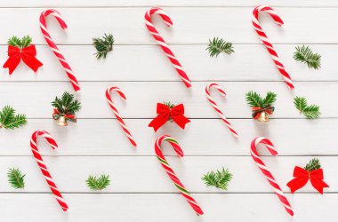 Bir kolaj, kırmızı yaylar ve ahşap bir yüzeyde küçük çanlar ile düzenlenmiş şeker kamışlarını gösterir. Yeşil çam dalları şenlikli görünümü artırır. Sahne, tatil süslemeleri ve kutlamaları temsil ediyor..