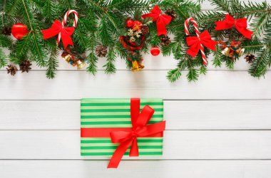 Beyaz ahşap bir yüzey üzerinde kırmızı bir kurdele ile yeşil bir hediye kutusunun üzerinde kırmızı kurdele, çam ve şeker kamışları bir tatil süslemeleri koleksiyonu içerir..