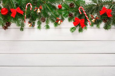 Dekoratif elementler tahta bir yüzeye yerleştirilir. Ürünler arasında kırmızı kurdeleler, kozalaklar, baston şekerler ve çanlar yer alıyor. Bu eşyalar kış tatili sezonunu simgeler ve şenlikli bir hava yaratır..