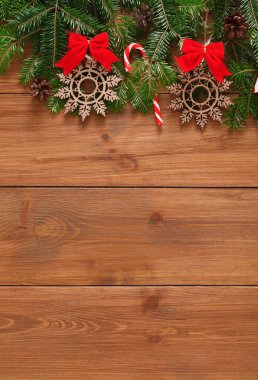 Tahta bir yüzeye kış süslemeleri sergileniyor. Yeşil çam dallarının yanında kar taneleri ve şeker kamışları yer alıyor. Kırmızı yaylar ekrana renk katar, neşeli bir görünüm yaratır.