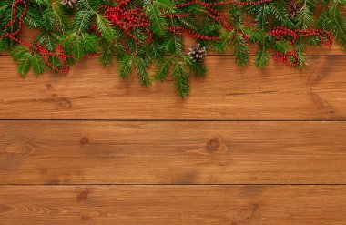 Tatil süslemelerinin bir koleksiyonu, tahta bir yüzey üzerinde kırmızı boncuklu ve çam kozalaklı çam dallarını gösteriyor. Bu düzenleme kış mevsiminde şenlik ruhunu vurgular..