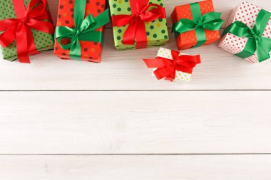 Kırmızı ve yeşil renklerde paketlenmiş hediye kutuları beyaz ahşap bir yüzeyde duruyor. Sahne, her kutunun üstünde fiyonklar olan şenlikli bir olay için düzenlendi..