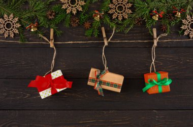 Üç paket hediye, mandallı bir ipte sergileniyor. Hediyeler kurdelelerle süsleniyor ve bir tatil teması için yeşil çam dallarının ve şenlikli süslemelerin üzerine yerleştiriliyor..