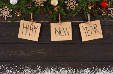 Tahta bir tahtanın üzerindeki mandallardan sarkan yılbaşı kutlamalarının yer aldığı bir kolaj. Gösteride çam dalları, süsler ve kar taneleri gibi şenlikli dekorasyonlar var..