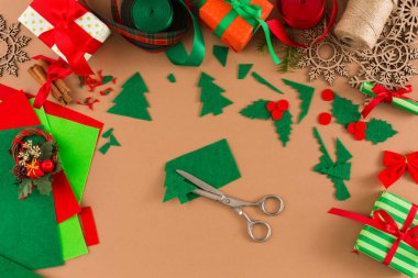 Çeşitli el sanatları malzemeleri masanın üzerine serilmiştir. Yeşil keçe ağaç şeklinde kesilmiş. Çalışma alanı etrafında kırmızı ve yeşil kurdeleler, ambalajlar ve dekorasyonlar düzenlenir. Makas ortaya konur..