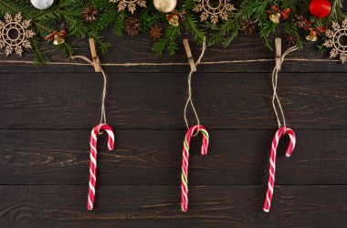 Üç tane baston şeker mandallı bir ipe asılıyor. İp, çam dalları, süsler ve ahşap kar taneleri gibi şenlikli eşyalarla süslenmiş. Bu sahne bir tatil temasını yakalar.