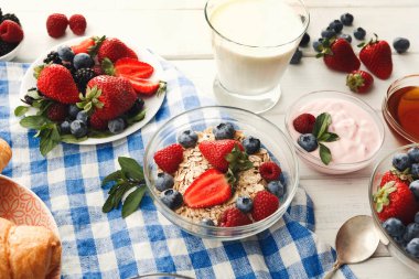 Sahne, kahvaltı malzemeleriyle dolu bir masa setini gösteriyor. Yoğurt, meyveli yulaf ezmesi tabakta taze böğürtlen ve bir bardak süt var..