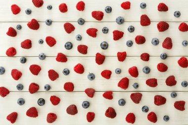 Ahududu ve yaban mersini ahşap bir yüzey üzerinde sıralanır. Kırmızı ve mavi meyveler basit bir kolaj oluşturuyor. Bu koleksiyon çeşitli şekil ve boyutları gösterir..